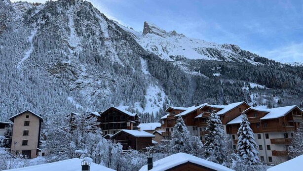 Un albergue de montaña con varias cabañas de madera, rodeado de árboles cubiertos de nieve y una montaña destacada al fondo.