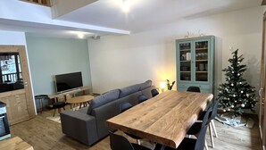 Una sala moderna con una mesa de comedor de madera, un sofá gris y un televisor pequeño.