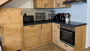 Cocina compacta con armarios de madera, microondas, cafetera y horno integrado.