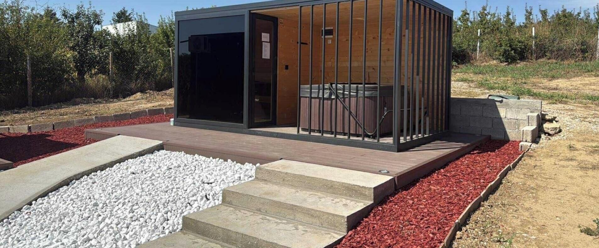 A modern outdoor structure with a wooden deck, a glass door, and a metal railing.