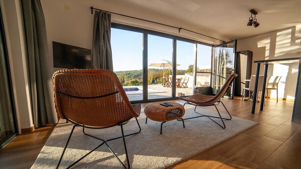 A spacious living area with large windows, a flat-screen TV, wicker furniture, and a view of the outdoors.