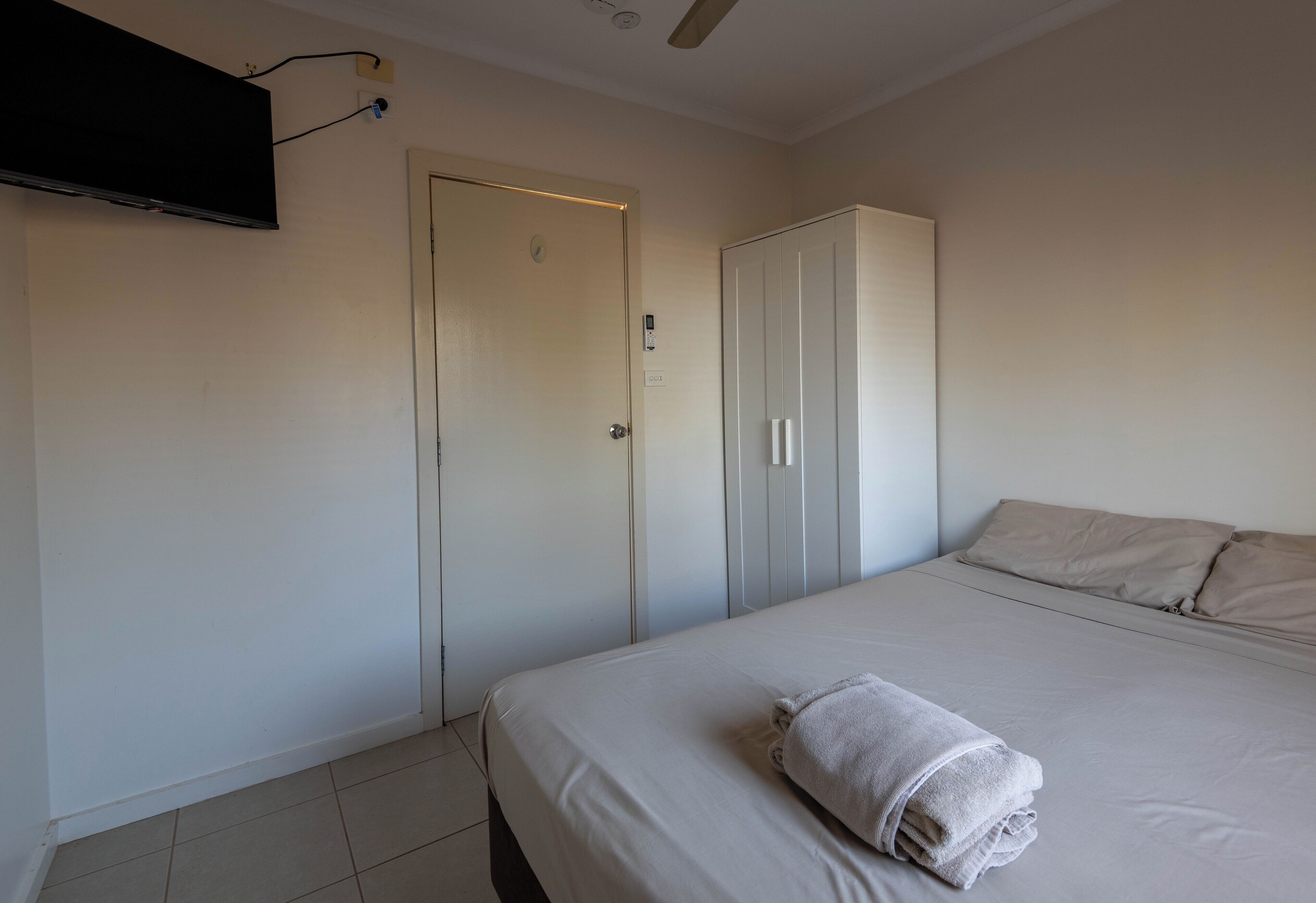A hotel room with a bed, a TV mounted on the wall, and a wardrobe.