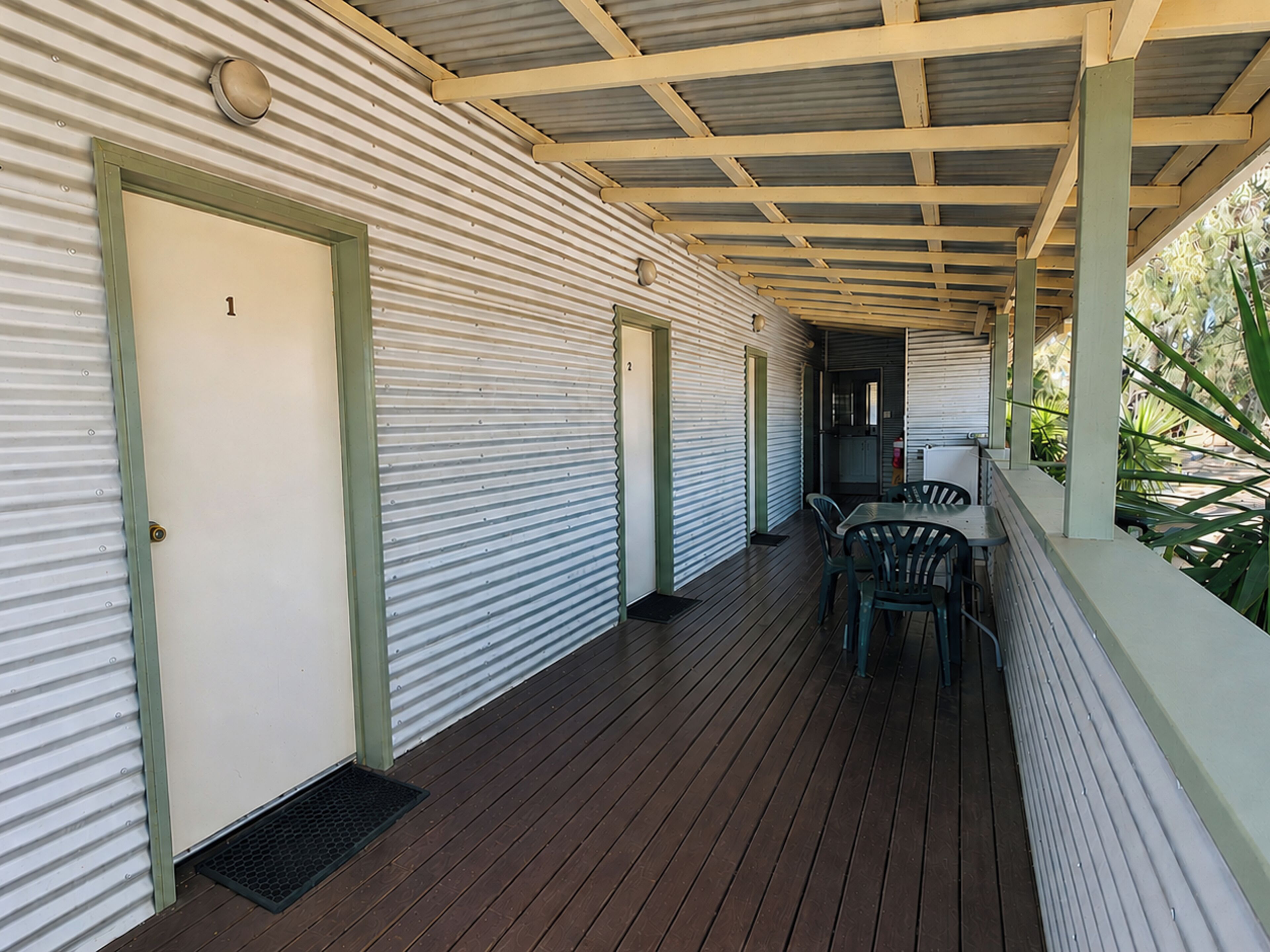 A covered outdoor area with a wooden deck, metal doors, and a seating arrangement.