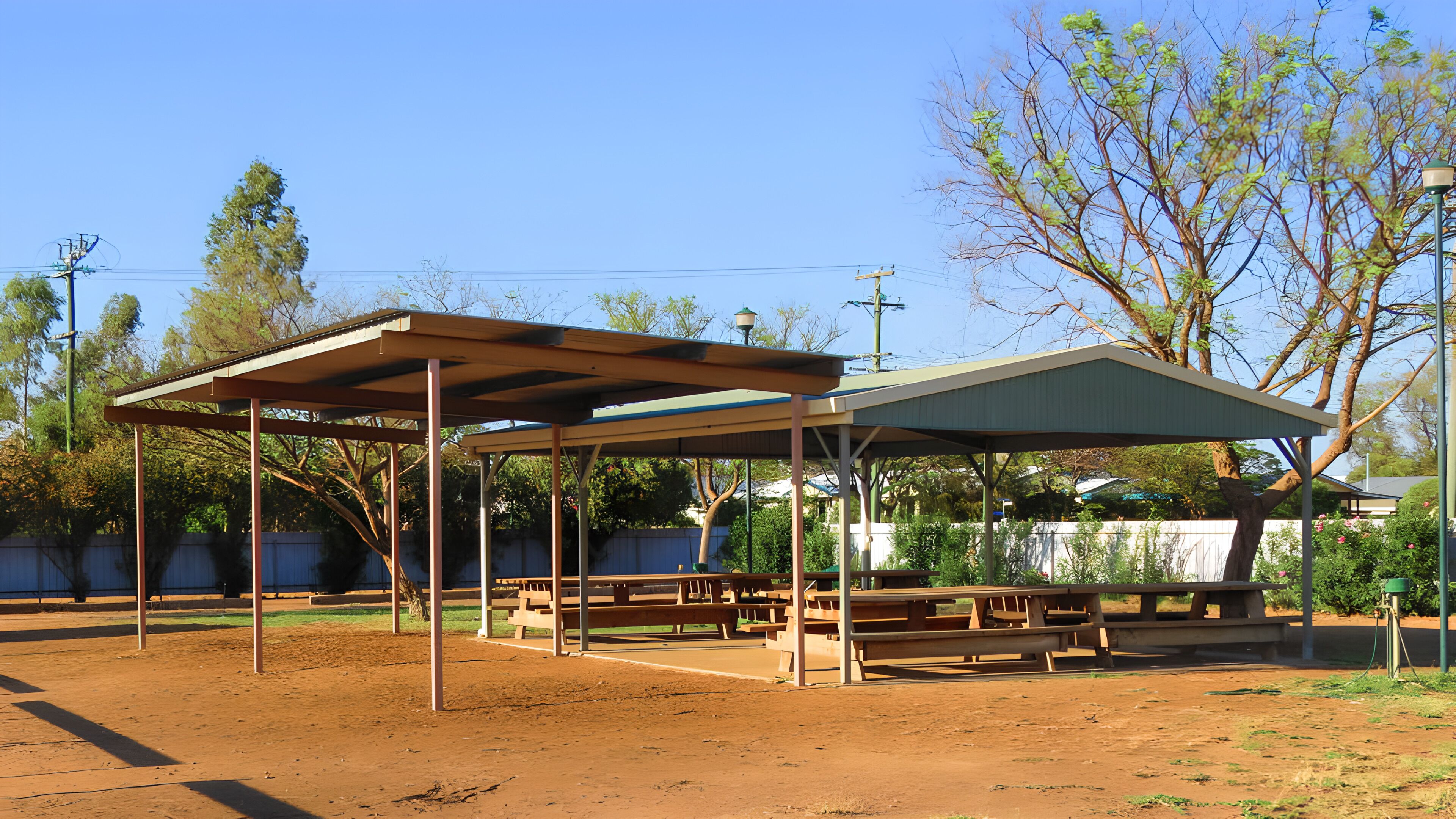 A covered picnic area with benches and tables, surrounded by trees and a fence.