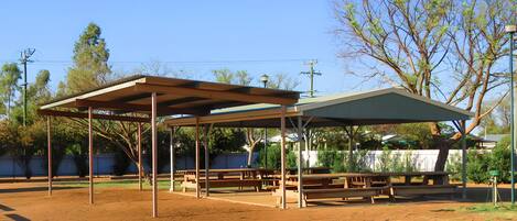 A covered picnic area with benches and tables, surrounded by trees and a fence.