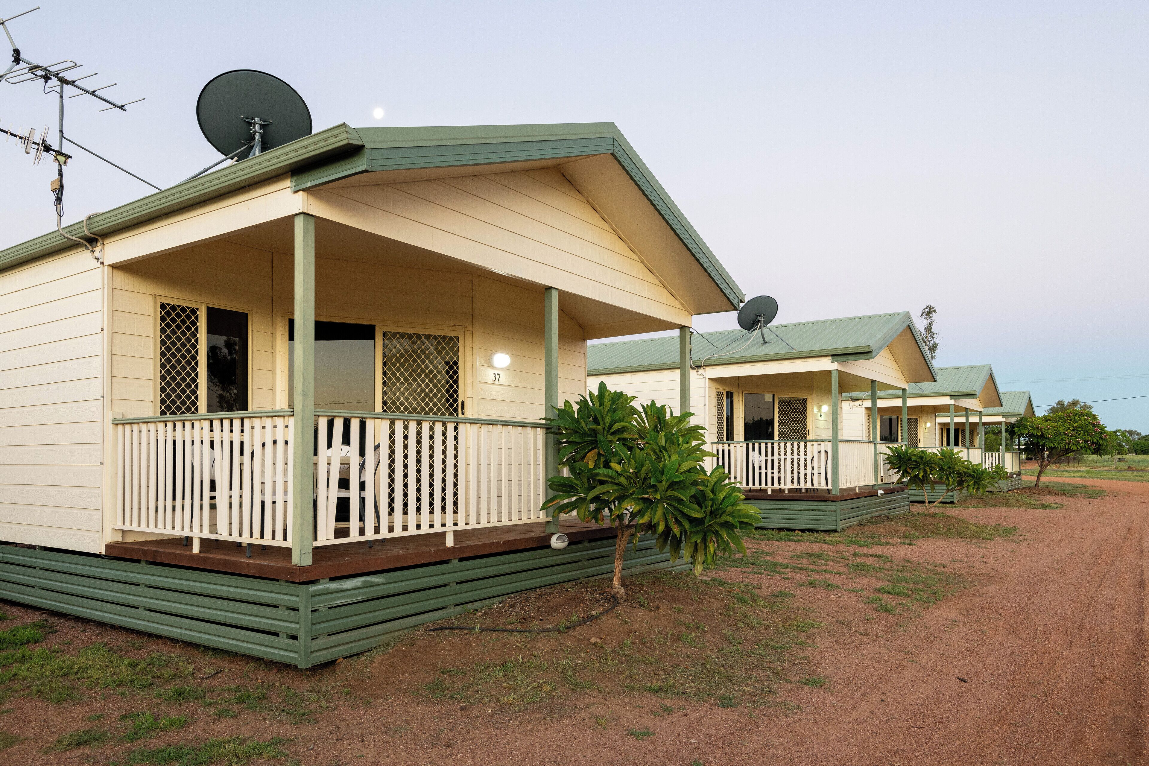 A row of identical, single-story cabins with green roofs and white walls, each featuring a porch with a railing.