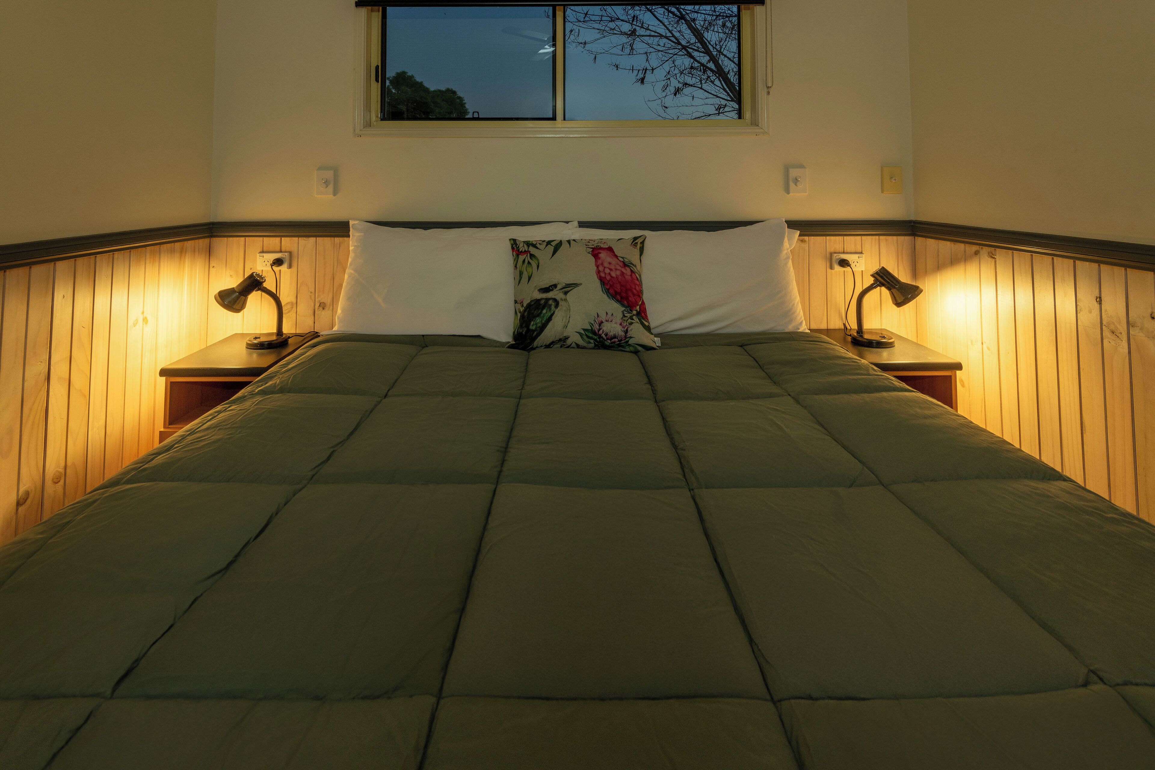 A bed with a green quilt, a floral pillow, and two bedside lamps.