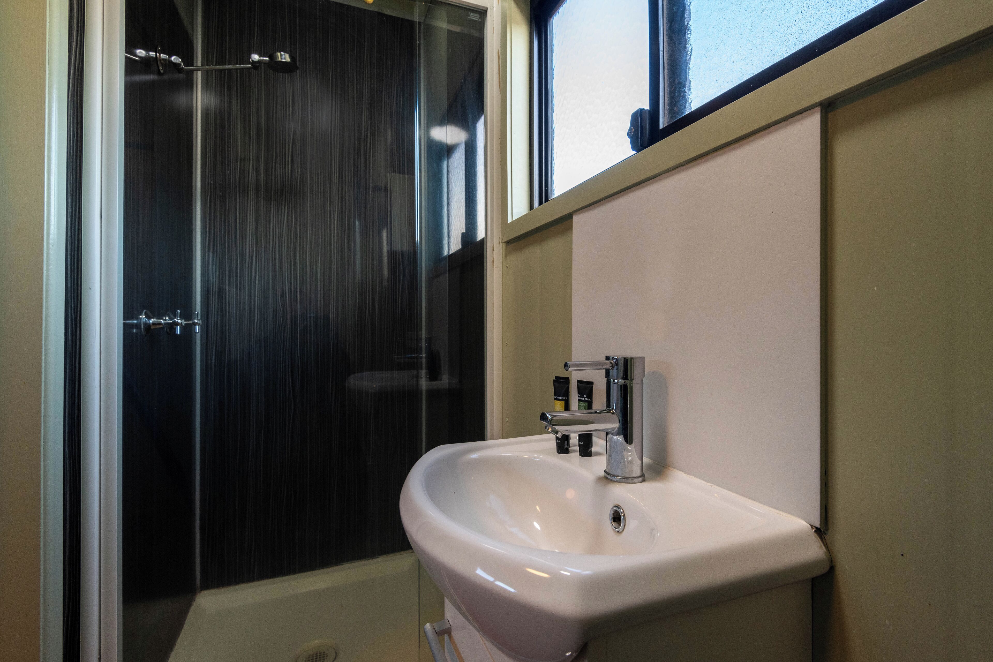 Un bany amb un lavabo blanc, un mirall i una zona de dutxa.