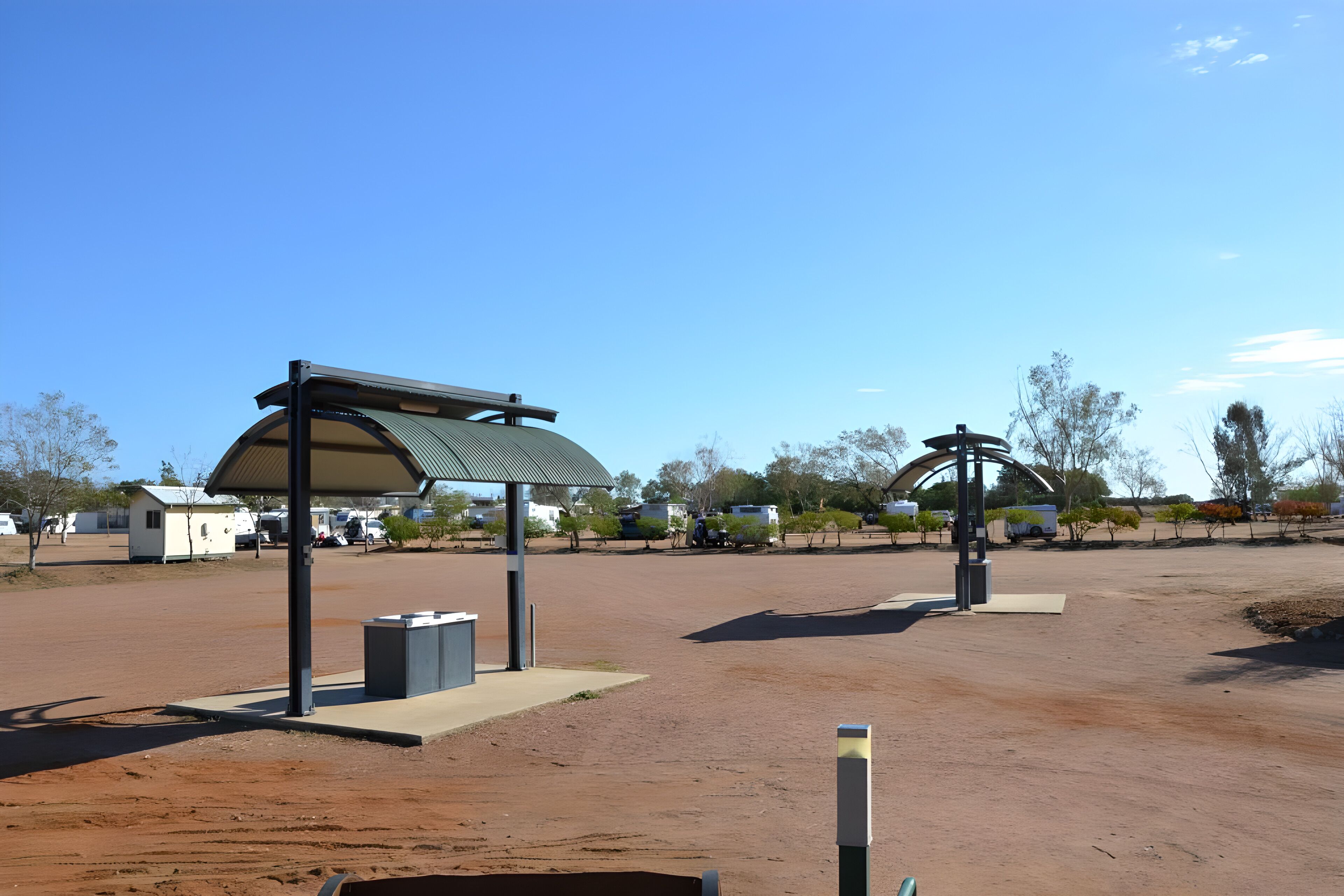 A parking area with a covered pavilion, a trash bin, and a kiosk.