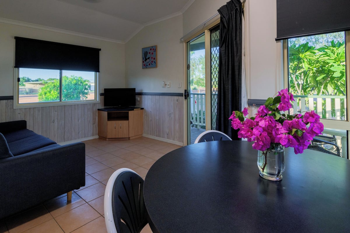 Una habitación con sofá, una mesa con sillas, televisor y ventana con vista a la vegetación.