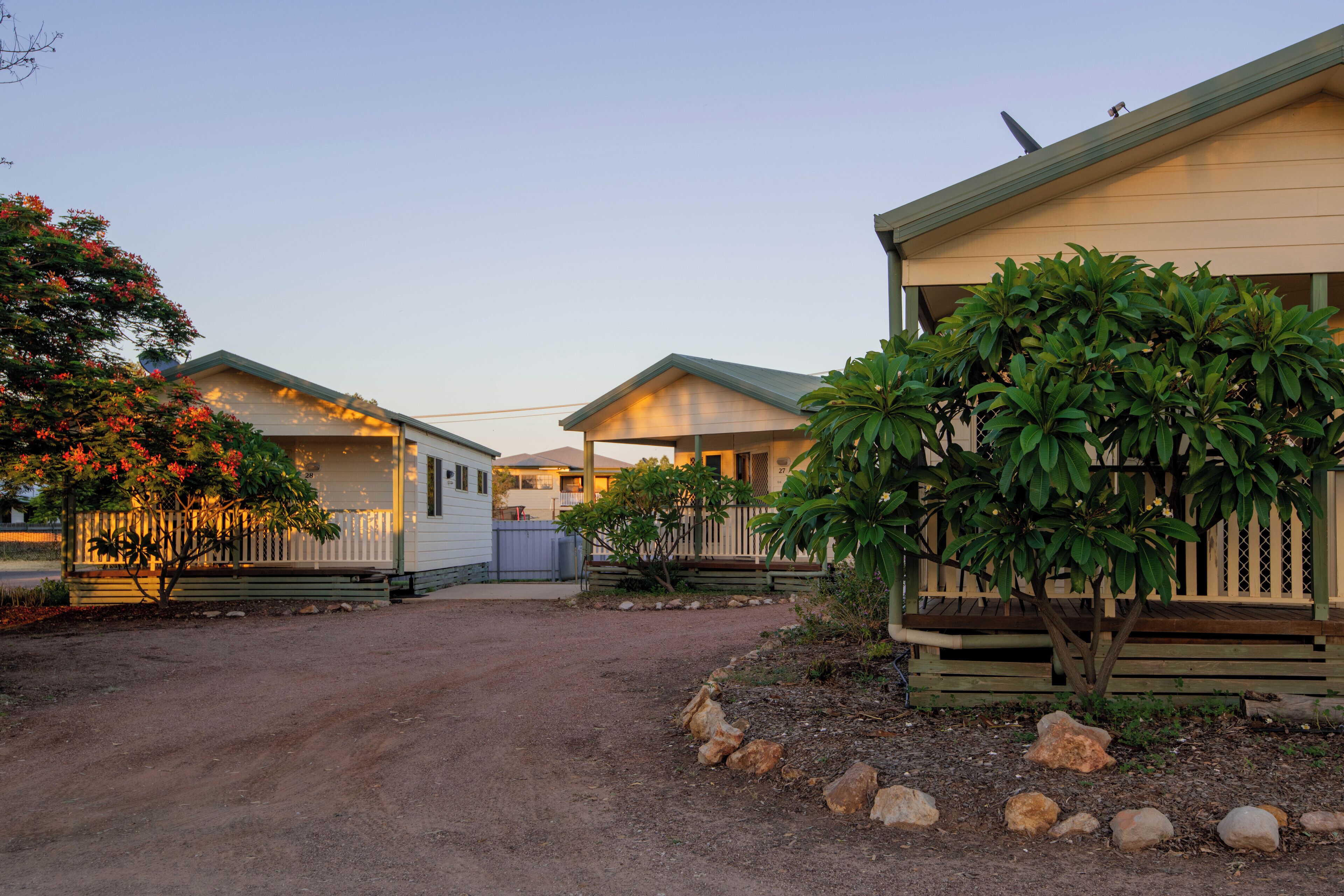 Une rangée de chalets de plain-pied, avec une allée en terre menant à l’entrée.