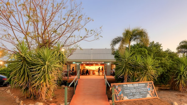 Ein Restaurant mit einer Holzterrasse, die zum Eingang führt, umgeben von tropischer Vegetation.