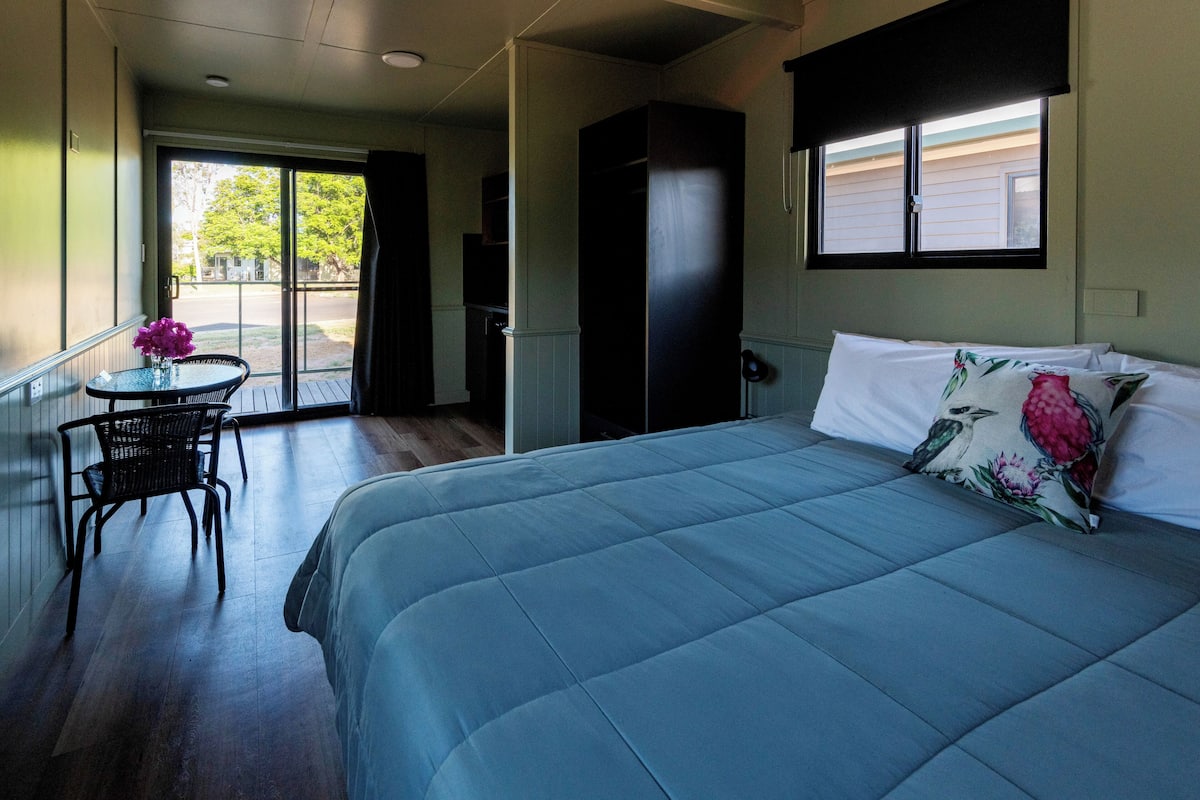 Un dormitorio con cama, una silla, una mesa y un armario.
