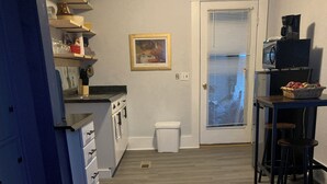 A kitchen with white cabinets, a sink, and a countertop. There is a trash can and a door with a window.
