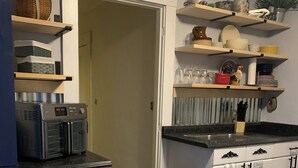 A kitchen with white cabinets, a black countertop, and wooden flooring. There are shelves above the counter holding various kitchen items.