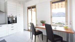 A modern kitchen with white cabinets, a built-in oven, and a dining area with two chairs and a table. - Lago 2 - Three Bedroom Apartment, Sleeps 8 (Oggebbio)