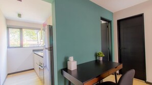Eine kleine Küche mit Kühlschrank, Fenster und einem Tisch mit einer Pflanze.