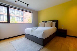 A bedroom with a bed, a nightstand, a lamp, and a window with a view of buildings. - TOP Escandon Double Bright 2BR Apartment (Mexico City)