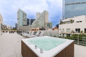 Une terrasse sur le toit avec un jacuzzi, des chaises longues et une vue sur la ville.