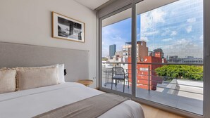 Een moderne hotelkamer met een groot bed, een ingelijst schilderij aan de muur en een balkon met uitzicht op de stad.