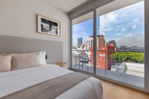 Une chambre d’hôtel moderne, dotée d’un grand lit, d’un tableau encadré au mur et d’un balcon offrant une vue sur la ville.