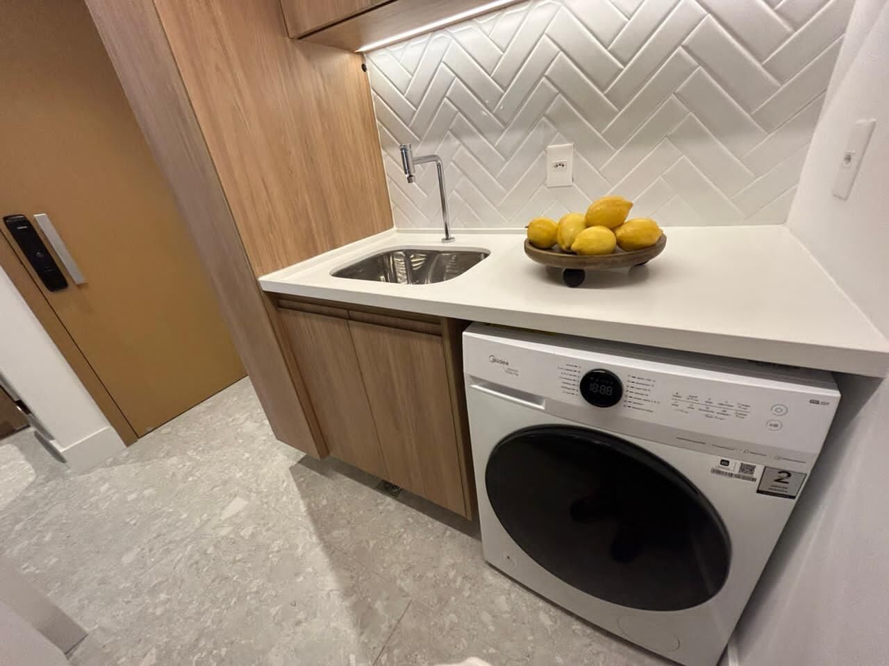 A compact kitchen with a built-in washing machine, a sink, and a bowl of lemons on the countertop.