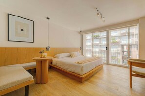 A modern bedroom with a wooden bed, a bench, a bedside table, and a large window with a view of buildings. - The Raven Exclusive Modern 2BR Apartment (Mexico City)