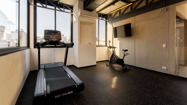Une salle de sport équipée d’un tapis de course, d’un vélo d’appartement et de grandes fenêtres donnant sur la ville.