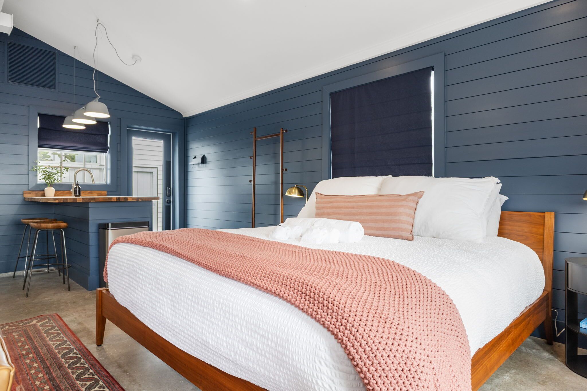 A bedroom with a large bed, a wooden headboard, a desk with a chair, and a window with blinds.