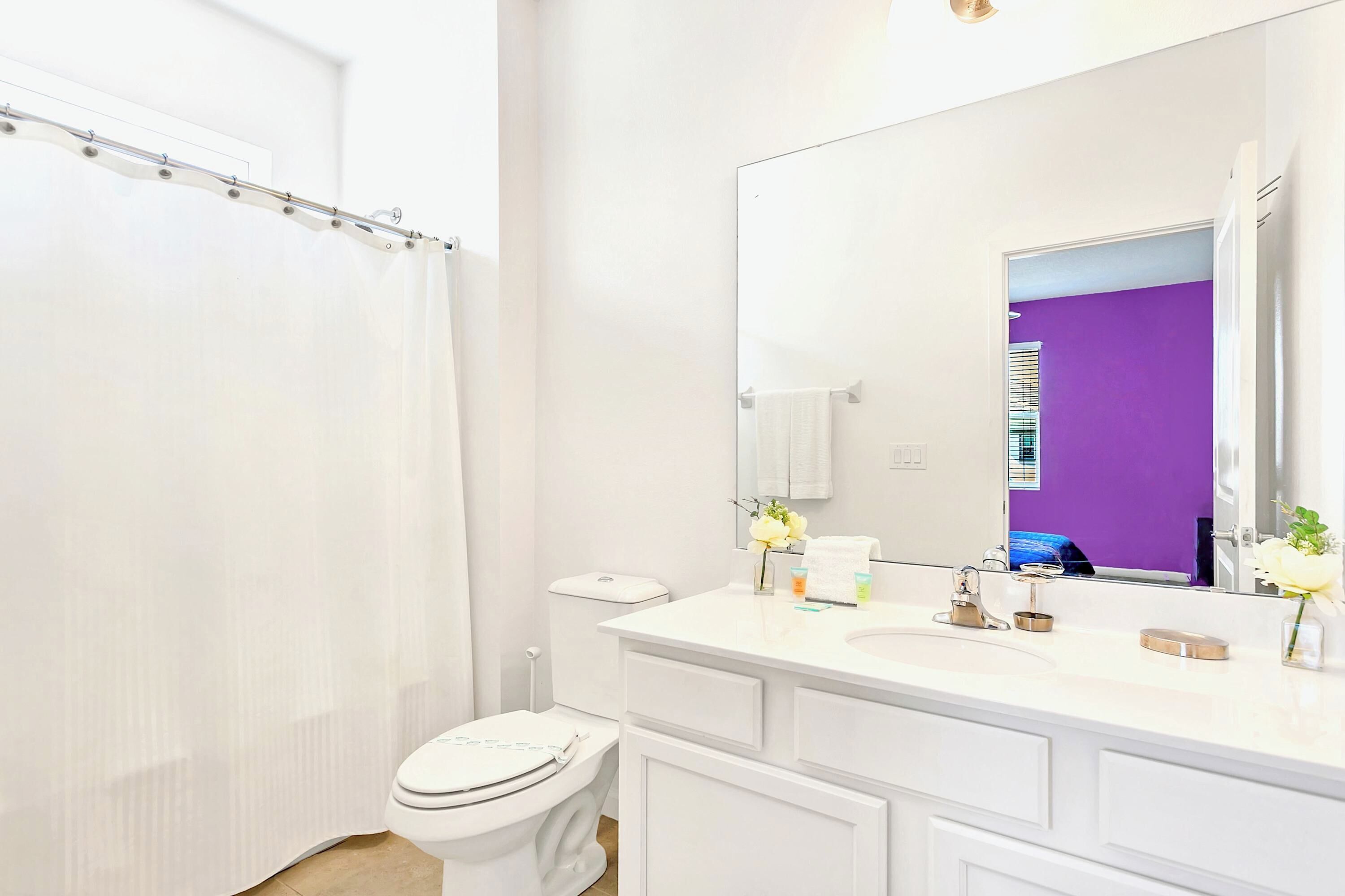 Un baño con inodoro y lavamanos blancos, y un espejo grande.