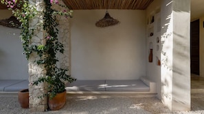 Un pilar de piedra con plantas trepadoras, una lámpara de techo tejida y un banco bajo un techo de paja.