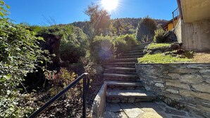 A stone staircase leading uphill with a metal handrail, surrounded by lush greenery and a clear blue sky.