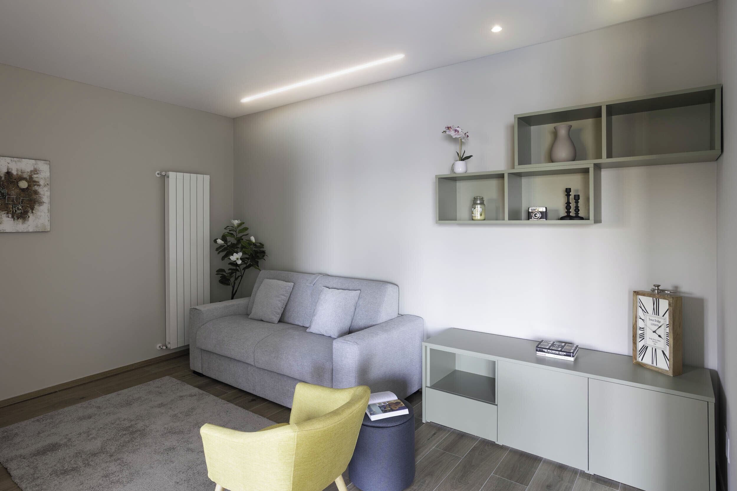 Ein modernes Wohnzimmer mit einem grauen Sofa, einem gelben Sessel, einem weißen Konsolentisch und einem grauen Teppich.