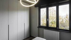 Ein modernes Schlafzimmer mit großem Fenster, einer runden Leuchte und Einbauschränken.