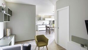 Ein modernes Wohnzimmer mit einer Couch, einem Essbereich mit Tisch und Stühlen sowie einer Küche im Hintergrund.