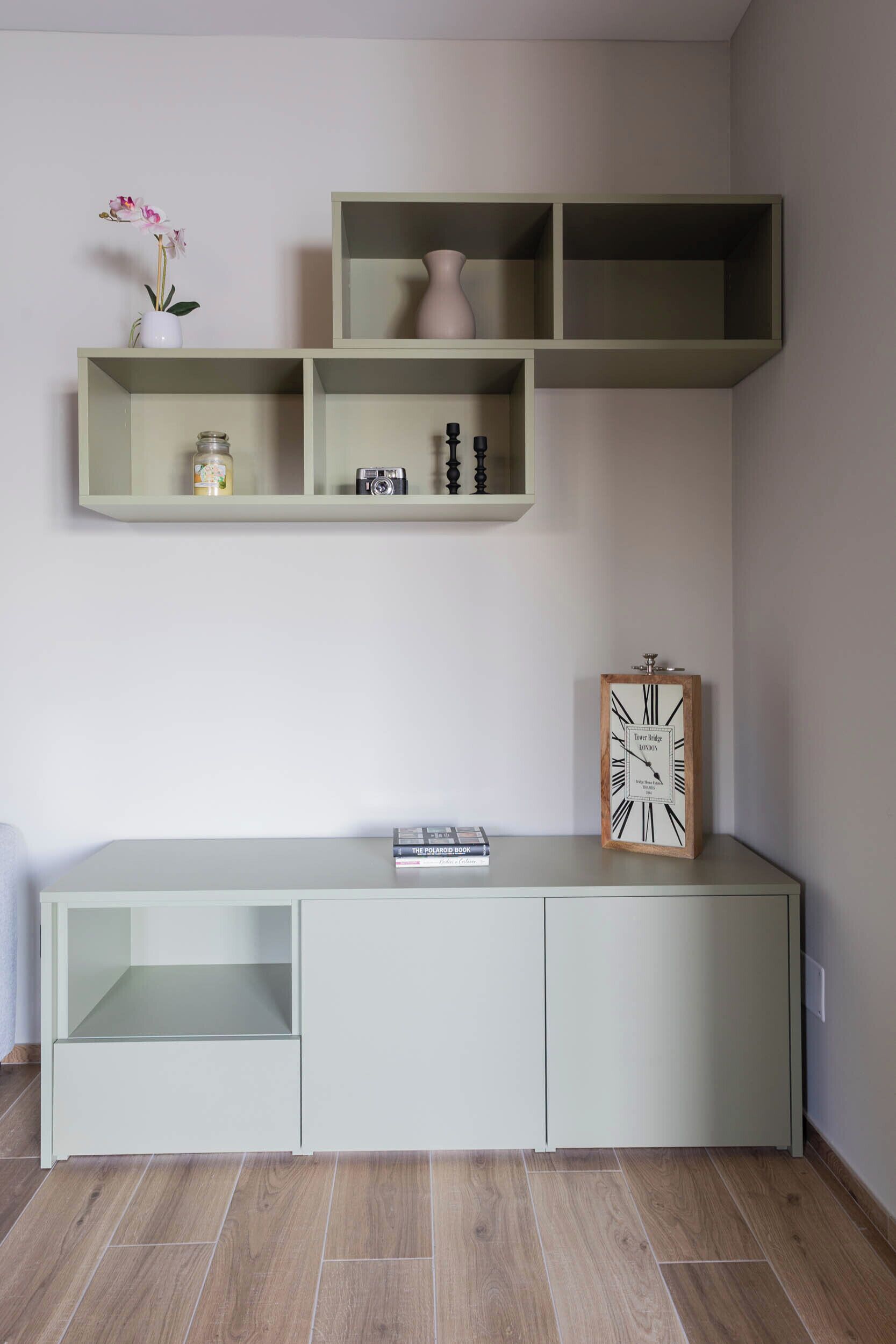 Habitació minimalista amb un moble de disseny verd clar, un rellotge i prestatges a la part superior.