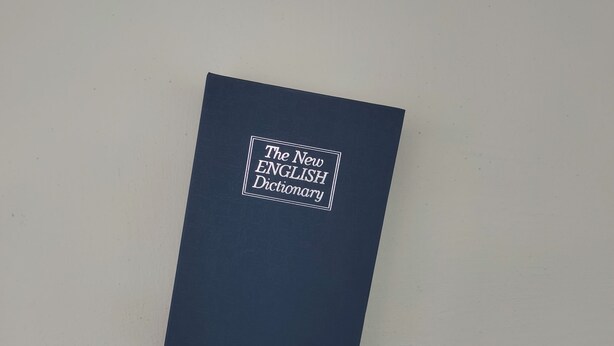 A closed book titled "The New English Dictionary" on a plain background. - Jess Oasis Stay Tambun (Ipoh)