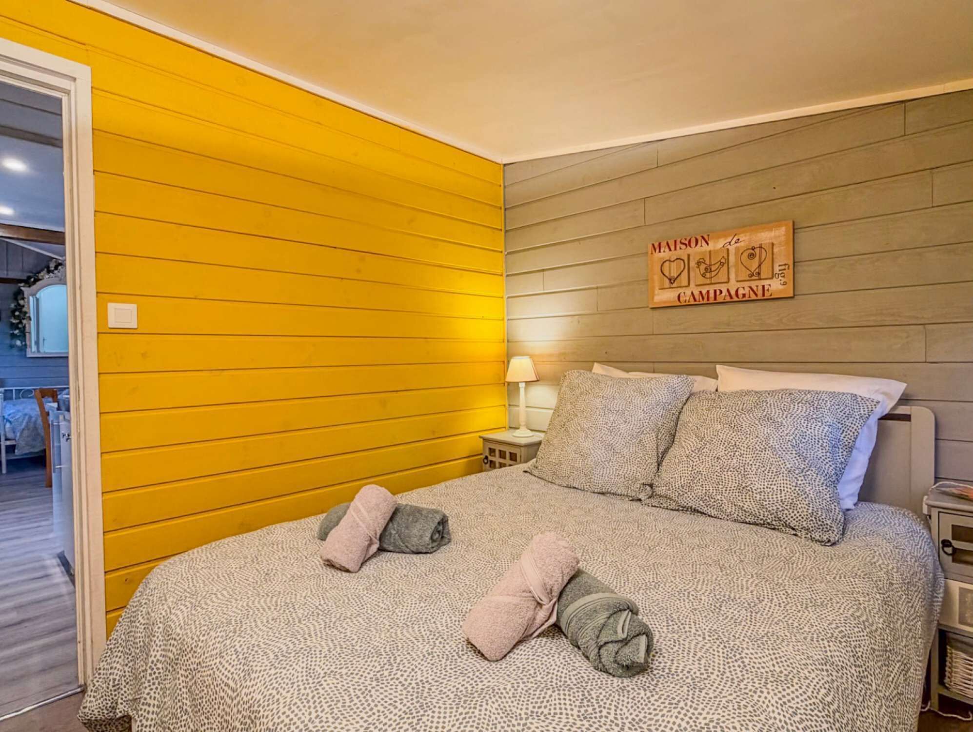 A bedroom with a bed, pillows, a nightstand, a lamp, and a wall sign.