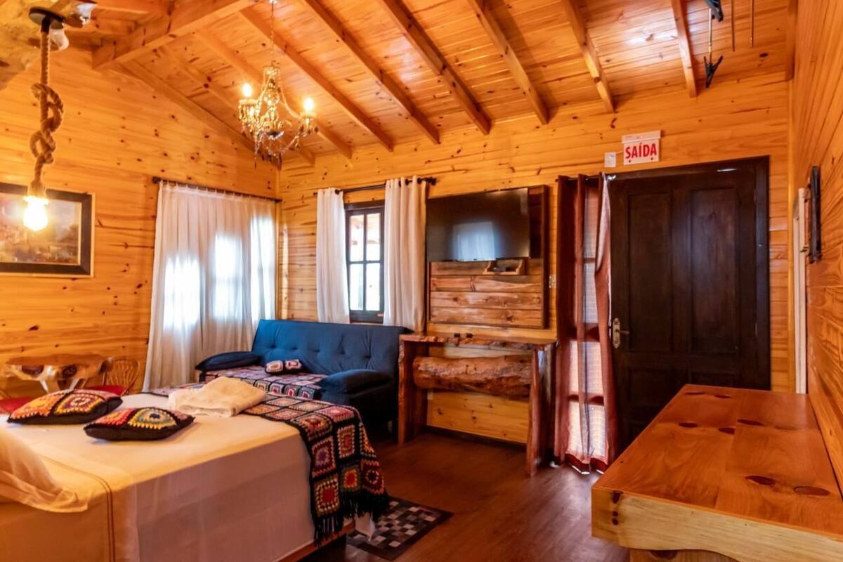 A cozy wooden cabin interior with a bed, sofa, and a dining table. A sign on the door reads "SAIDA".