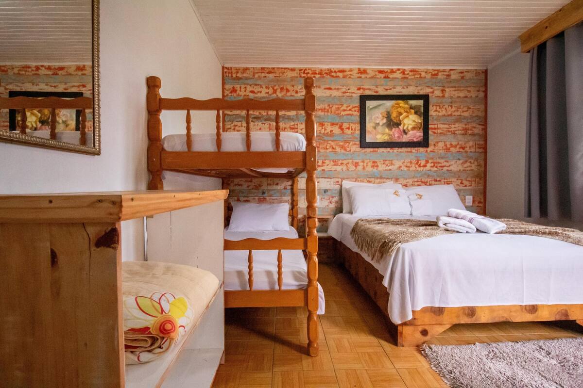 A room with a bunk bed, a single bed, wooden furniture, and a floral wall decoration.