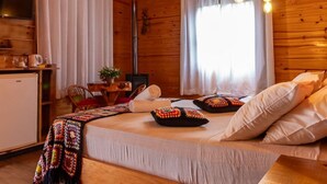 A cozy wooden cabin room with a bed, a chandelier, and a dining area. - Hospedagem Rural Recanto do Riacho (Urubici)