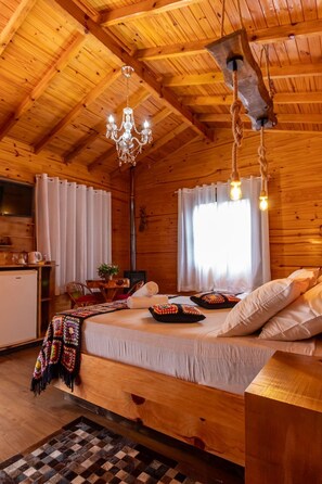 A cozy wooden cabin room with a bed, a chandelier, and a dining area. - Hospedagem Rural Recanto do Riacho (Urubici)
