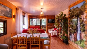 A cozy room with a wooden ceiling, a dining table with chairs, a red sofa, a TV, and a wall with a waterfall mural. - Hospedagem Rural Recanto do Riacho (Urubici)