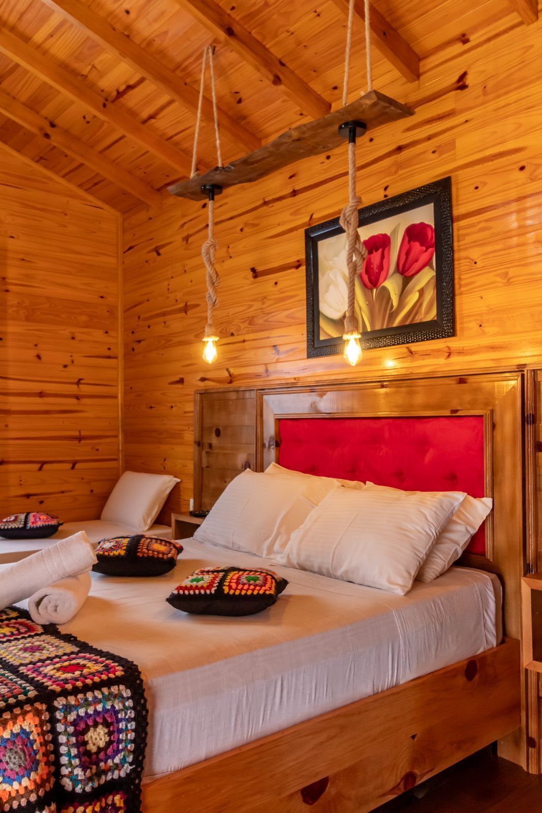 Quarto de cabana de madeira com cama, cabeceira vermelha e quadro com flores na parede.