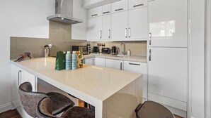 Una cocina moderna con gabinetes blancos, una campana extractora de acero inoxidable y una isla central con taburetes de bar.