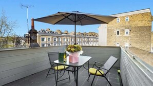 Terraza en la azotea con una mesa, sillas, un arreglo floral y vistas a casas escalonadas.