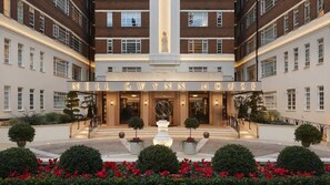The exterior of Nell Gwyn House, featuring a symmetrical facade with a central entrance, a fountain, and a well-maintained garden with red flowers. - Glamorous Art Deco Flat in Chelsea (Greater London)