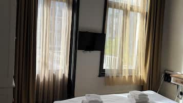 Habitación de hotel con cama, dos ventanas con cortinas, un televisor de pantalla plana y una mesita con utensilios de cocina.