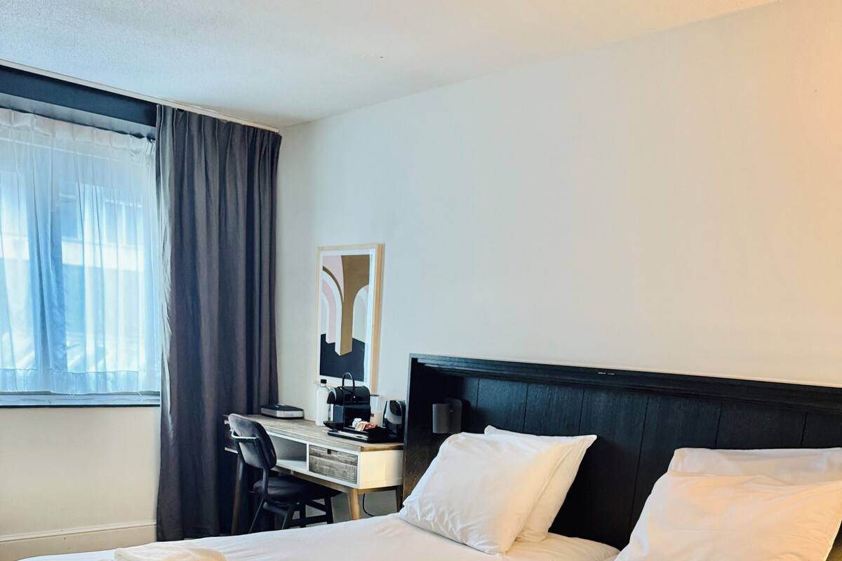 Une chambre d’hôtel avec un grand lit, un bureau, une chaise et une fenêtre avec des rideaux.