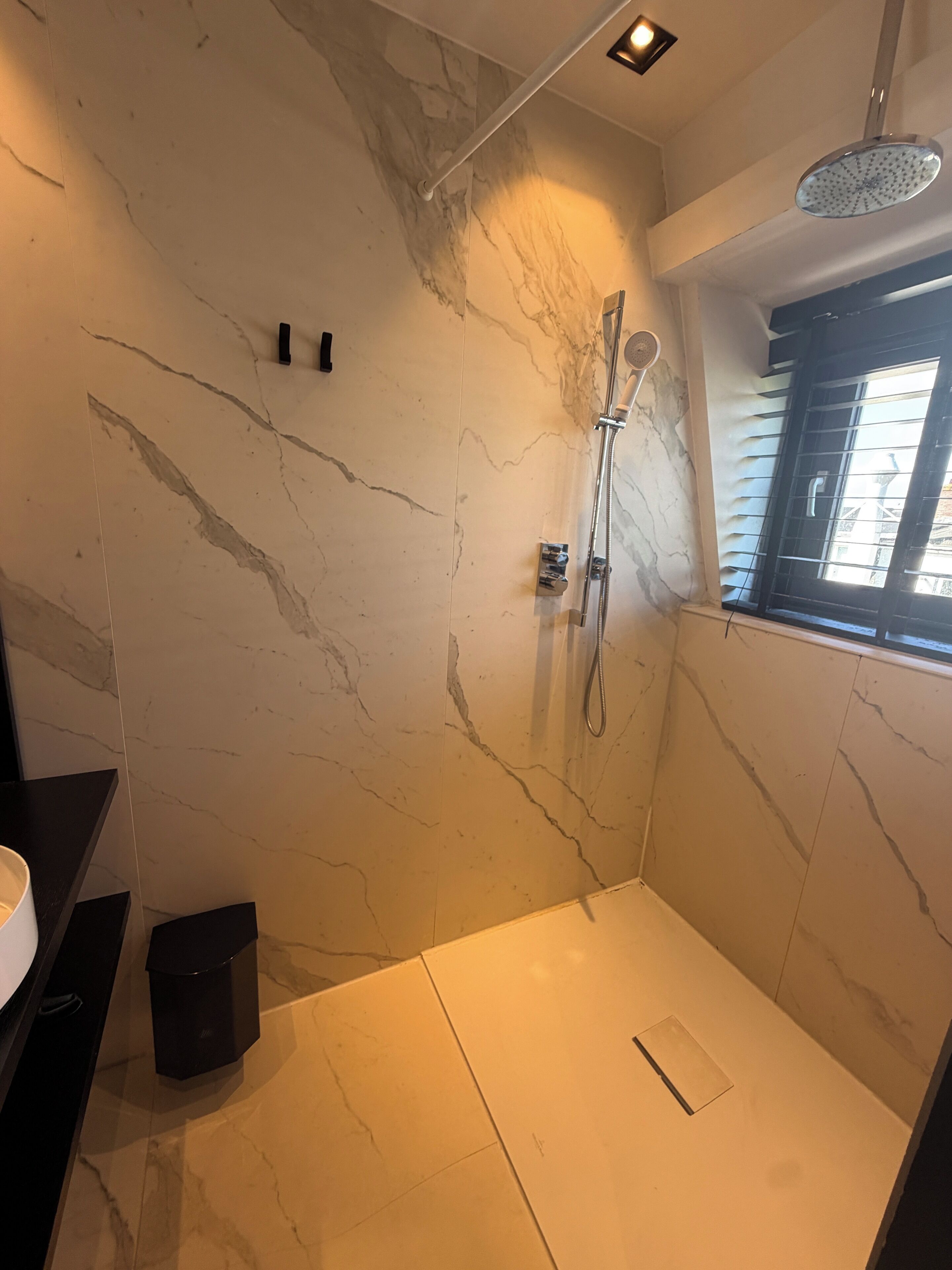 A modern bathroom with a shower, marble walls, and a window.
